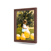 A young girl in a white dress is surrounded by yellow balloons in a grassy outdoor setting.
