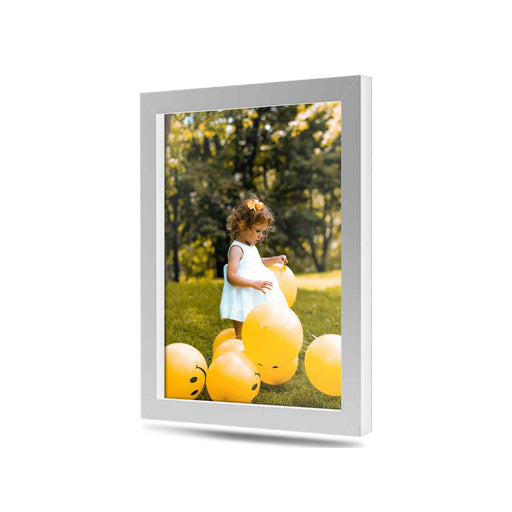 A young girl in a white dress is surrounded by yellow balloons in a grassy outdoor setting.
