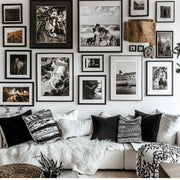 a cozy living room with a white couch adorned with patterned throw pillows and a white blanket. The walls are decorated with a collection of framed black and white photographs, creating a visually appealing gallery-like display.