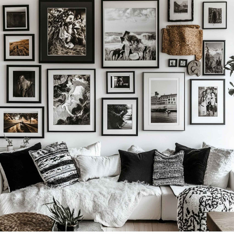 a cozy living room with a white couch adorned with patterned throw pillows and a white blanket. The walls are decorated with a collection of framed black and white photographs, creating a visually appealing gallery-like display.